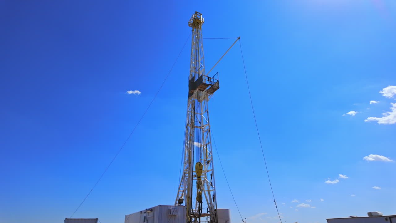 Coming up to the equipment for natural resources boring. Low angle view at the derrick producing oil.