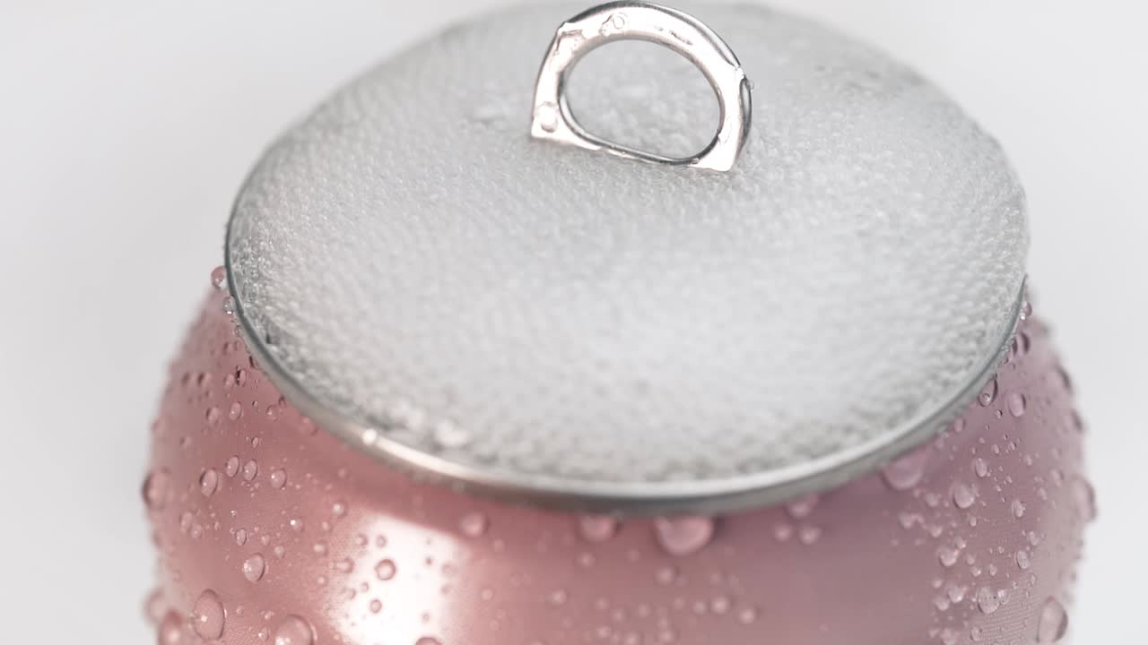 lata de soda rosa fría agitada abierta a cámara lenta llena de burbujas llenando la tapa