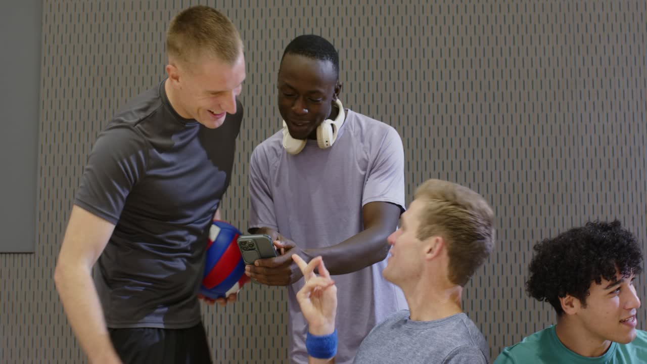 5 compagni di squadra maschi che si riuniscono su una panchina, un uomo afroamericano tira fuori lo smartphone mostrando un video.