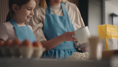 funny girl and her mother are cooking and having fun in kitchen preparing dough and smearing each other nose with flour