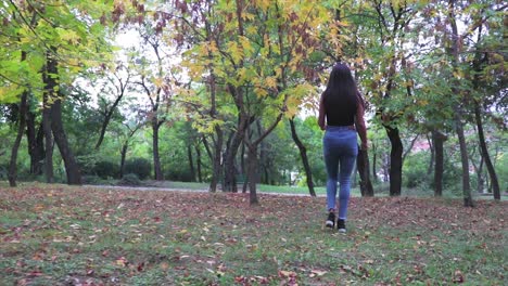 Beautiful-hot-girl-walking-through-a-park-with-green-trees-low-angle-shot