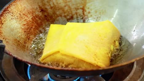 a yellow parcel is deep-fried in a wok over a blue flame, sizzling in hot oil.
