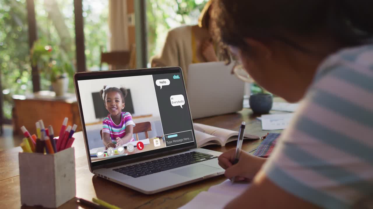 Schoolgirl using laptop for online lesson at home, with girl talking and web chat on screen