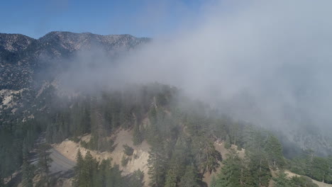 slow push in drone shot of fog rolling over a mountain top and a winding road