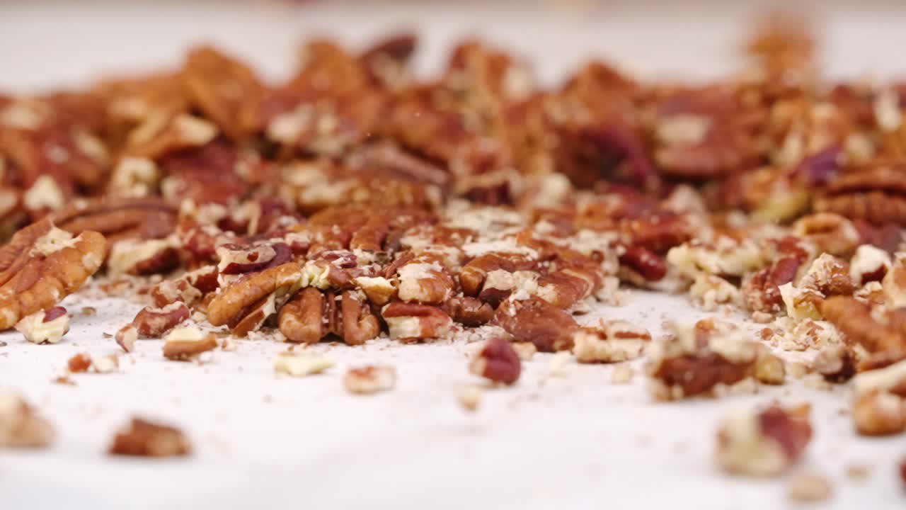 Whole pecan nuts being broken into tiny crushed pieces by mallet in slow motion