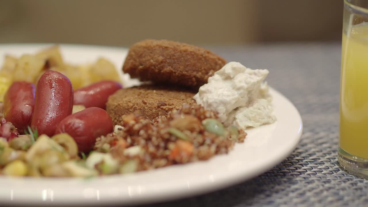 Primo piano di un piatto da colazione vario con salsicce, falafel, mais e insalata