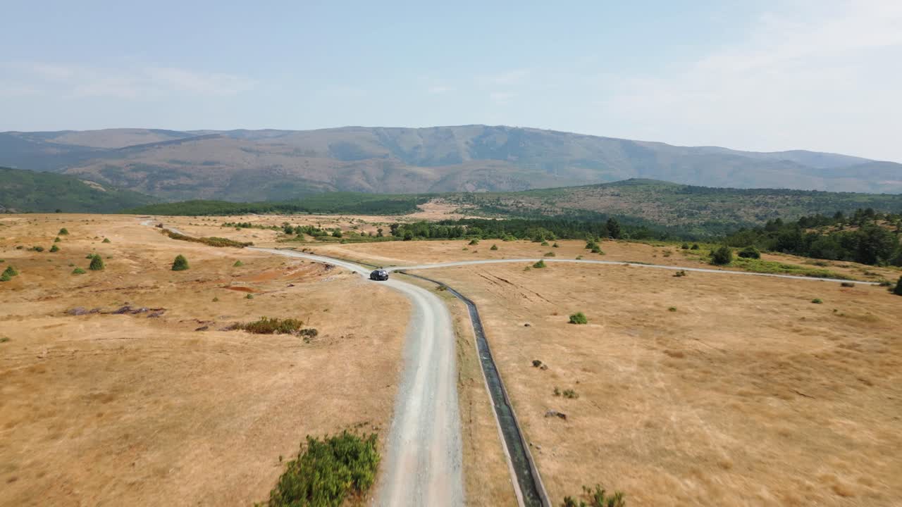 Car driving through dry countryside with mountains in the background on a sunny summer day in Albania. Scenic road trip and travel adventure footage