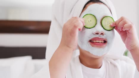 Video-of-happy-asian-girl-in-robe-doing-cucumber-mask-and-having-fun