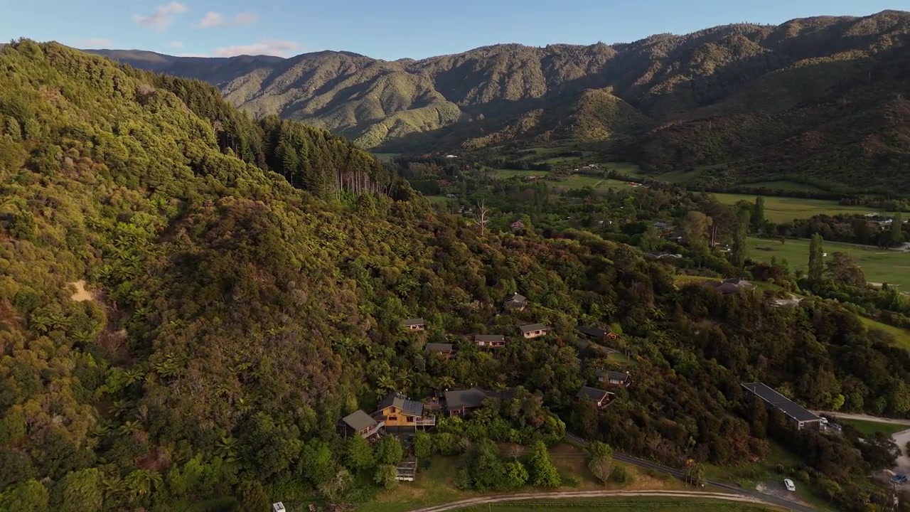 Vista de drone de casas e propriedades isoladas aninhadas em uma floresta verde exuberante nas encostas de Marahau ao pôr do sol na Nova Zelândia.