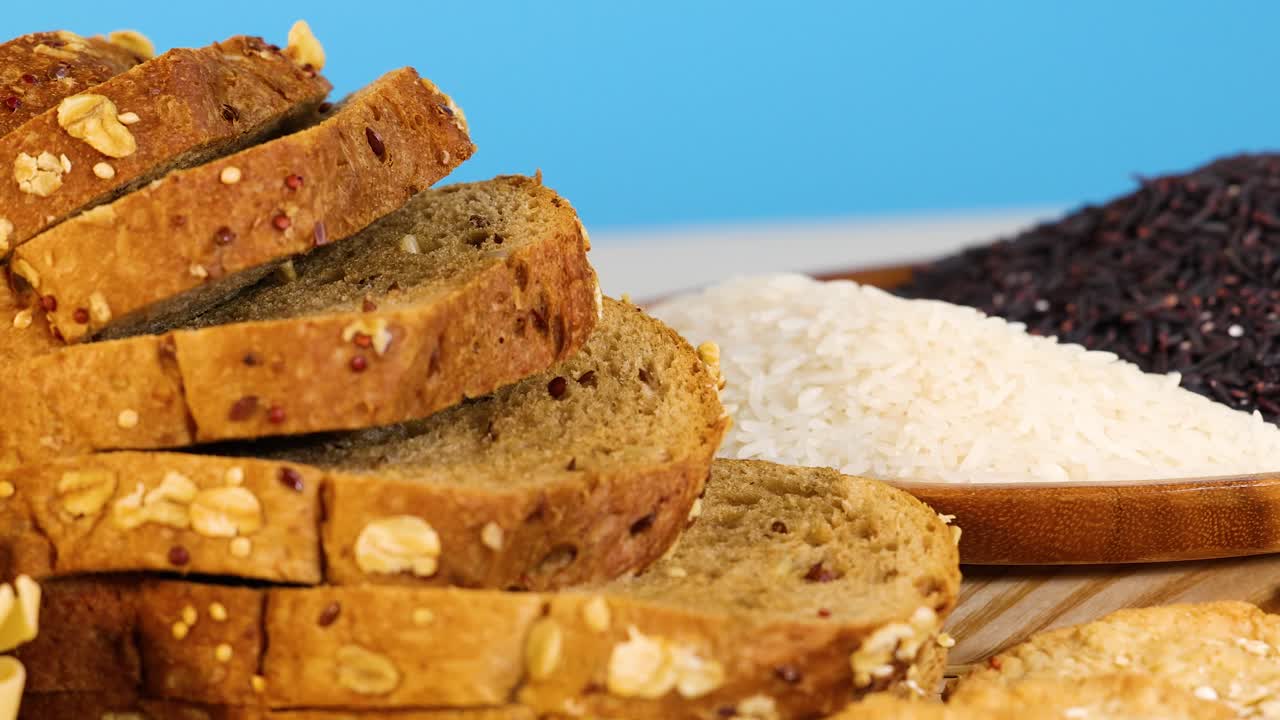 A colorful arrangement of grains, sliced bread, and pasta against a bright blue background, showcasing diverse food textures