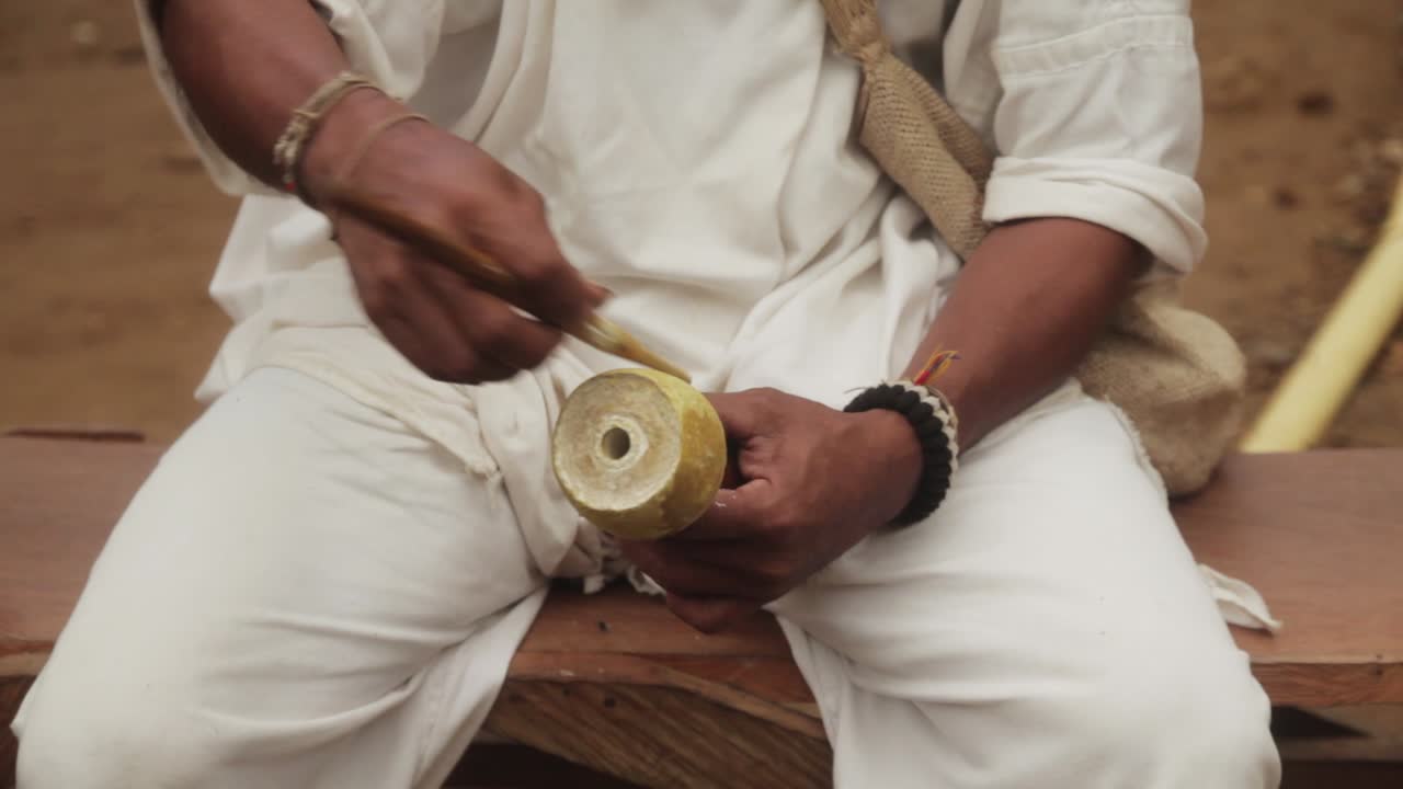 Close-up of the hands of an Aruhaco man holding a poporo and chewing coca leaves