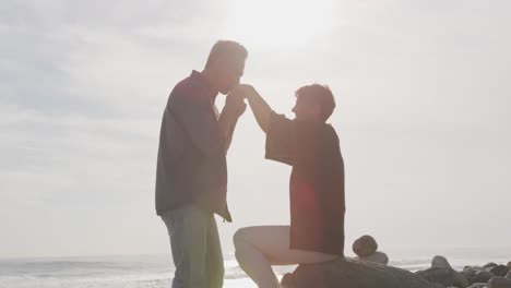 caucasian couple enjoying free time by sea on sunny day, man kissing hands