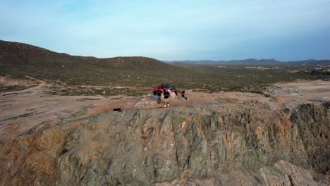 friends with their dogs standing on a seaside cliff, sunset in cabo, mexico - aerial view