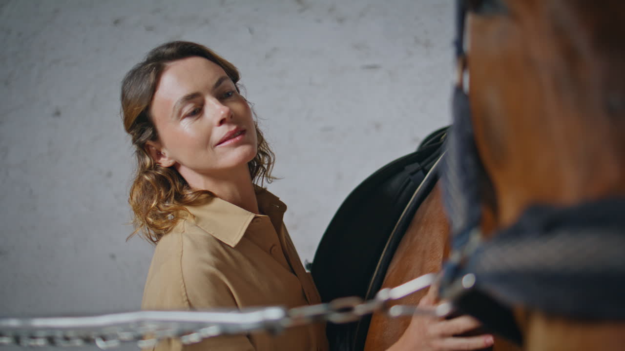 Lady jockey stroking horse fur at cozy paddock closeup. Woman touching animal