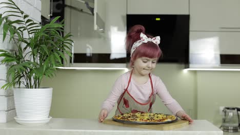 cocinando pizza. niño pequeño en delantal con pizza caliente recién horneada en la cocina