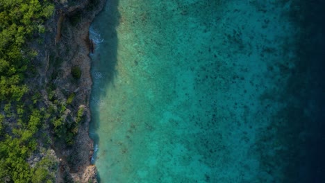 Drone-De-Arriba-Hacia-Abajo-A-Través-De-Un-Alto-Acantilado-Tropical-Caribeño-Mientras-Las-Nubes-Se-Mueven-Y-La-Luz-Del-Sol-Se-Extiende-Sobre-Los-Arrecifes-De-Coral