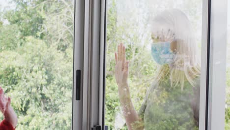 Mother-and-daughter-wearing-face-masks-touching-each-other-through-the-glass