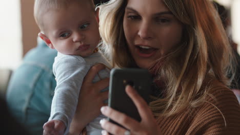 Madre-Joven-Con-Bebé-En-La-Cafetería-Usando-Un-Teléfono-Inteligente-Tomando-Café-Relajándose-En-Un-Restaurante-Concurrido-Disfrutando-De-La-Maternidad