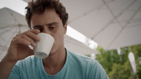 de cerca joven leyendo y bebiendo café bajo las grandes sombrillas blancas de verano