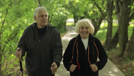 Active-senior-old-couple.-Man-training-Nordic-walking,-woman-running-in-park