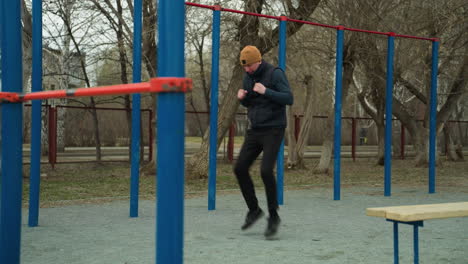 a coach jogs briskly in a stadium, surrounded by blue and red poles, with a bench nearby, with barren trees and passing cars and people visible in the background