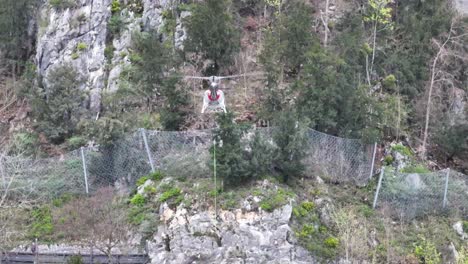 Helicopter-in-action-near-rocky-cliff,-securing-area-with-cables-at-Walensee,-Switzerland