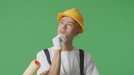 Close Up Of Asian Man Painter Wearing Safety Helmet Thinking About Something And Looking Around While Standing In The Green Screen Background Studio