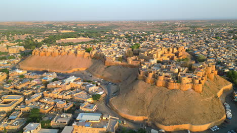 an elevated drone shot of jaisalmer fort, showcasing its majestic golden sandstone architecture, surrounded by traditional houses under a bright sunny sky in rajasthan's desert city, india. 4k.