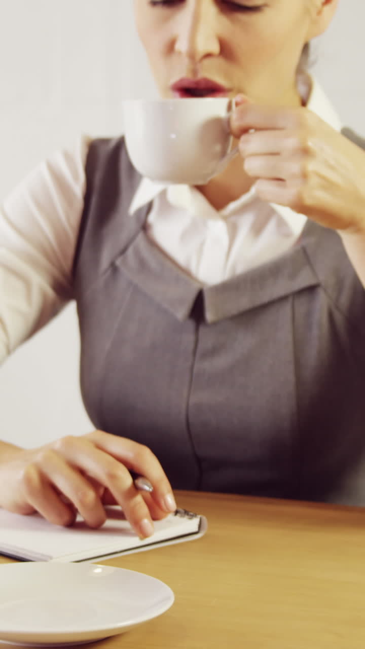 una mujer de negocios seria escribiendo notas mientras bebe café.