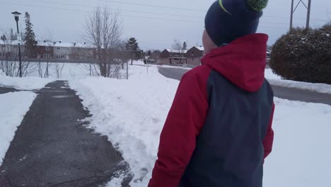 Niño-Pequeño-Caminando-Por-Un-Camino-Despejado-En-Invierno-Con-Chaqueta-Roja-Y-Blanca-Y-Toque-Azul-Con-Un-Pompón