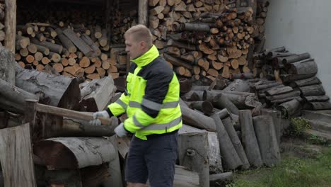 Lumberjack-in-reflective-jacket.-Man-woodcutter-hold-huge-axe.-Sawn-logs,-firewood-background