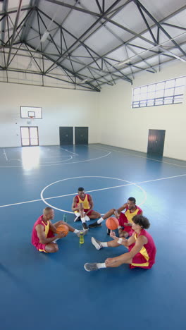 vertical video: basketball players sitting on court, resting and hydrating during practice