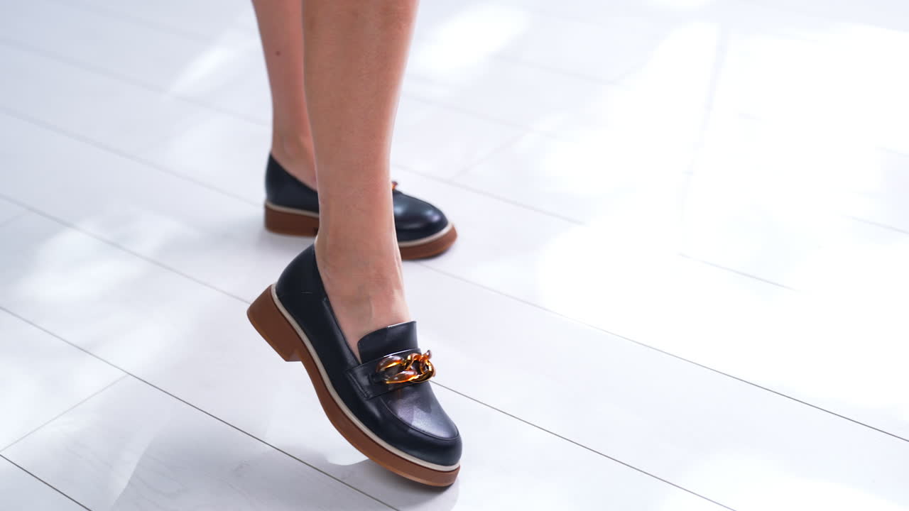 Beautiful black shoes on brown soles with chain decoration. Fashionable loafers on model's feet. Close up. White backdrop.
