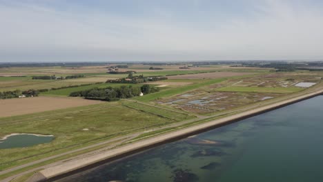 Aerial-shot-of-farmland-behind-a-dike-in-Zeeland,-the-Netherlands,-on-a-sunny-summer-day