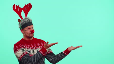 Man-wears-red-New-Year-sweater-deer-showing-thumbs-up-and-pointing-at-on-blank-advertisement-space