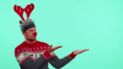 man wears red new year sweater deer showing thumbs up and pointing at on blank advertisement space