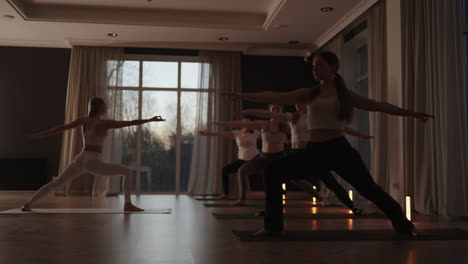 Group-of-young-woman-practicing-yoga-with-the-help-of-an-instructor.-They-are-doing-seated-side-twist-asana.-In-a-bright-room.