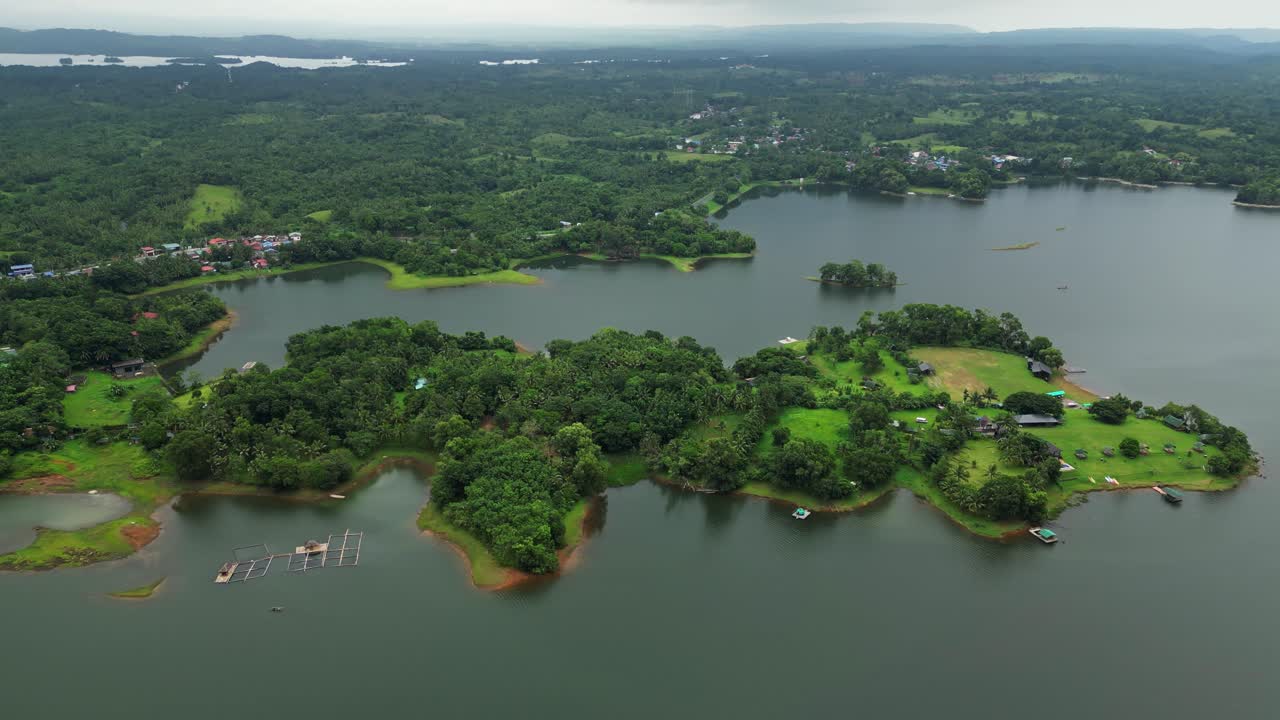 A wide drone shot starts from afar, slowly moving toward lush green land surrounded by water—creating a gentle approach highlighting harmony of land and water in Laguna