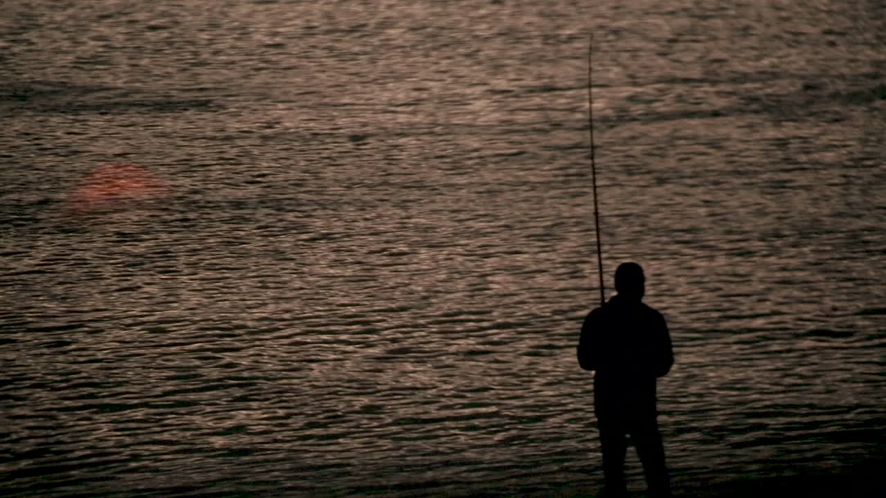 Seorang pria sedang memancing ikan saat senja di Selandia Baru.