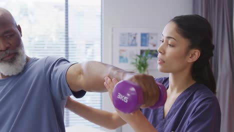 fisioterapeuta femenina diversa y paciente masculino de alto nivel sosteniendo una mancuerna en una sesión de fisioterapia