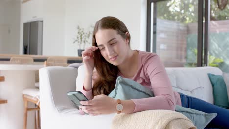 Happy-caucasian-woman-lying-on-couch-and-using-smartphone-in-slow-motion