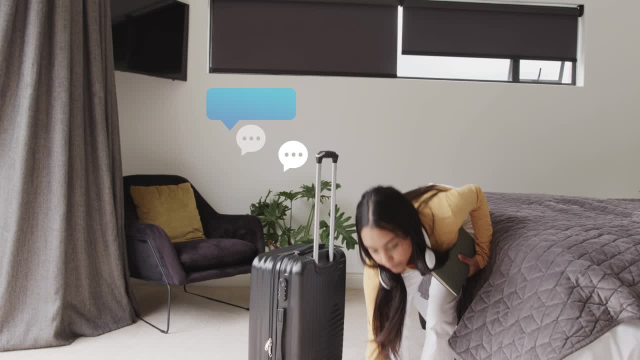 Woman packing suitcase by bed, responding to chat-bubble notifications while preparing travel
