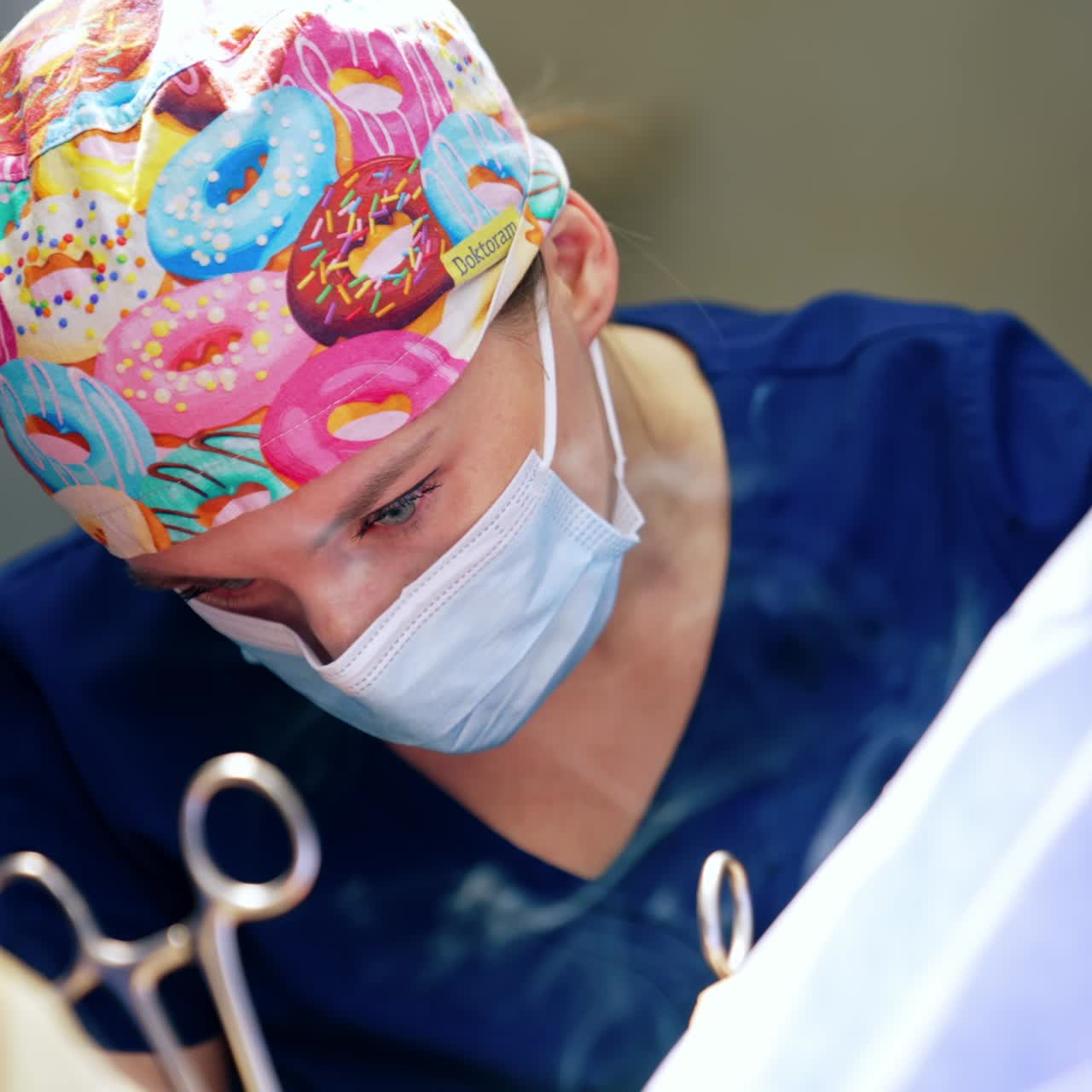 Caucasian female surgeon in bright cap uses device producing smoke. Portrait of a focused doctor performing surgery