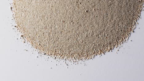 Video-of-close-up-of-heap-of-sand-grains-and-copy-space-on-white-background