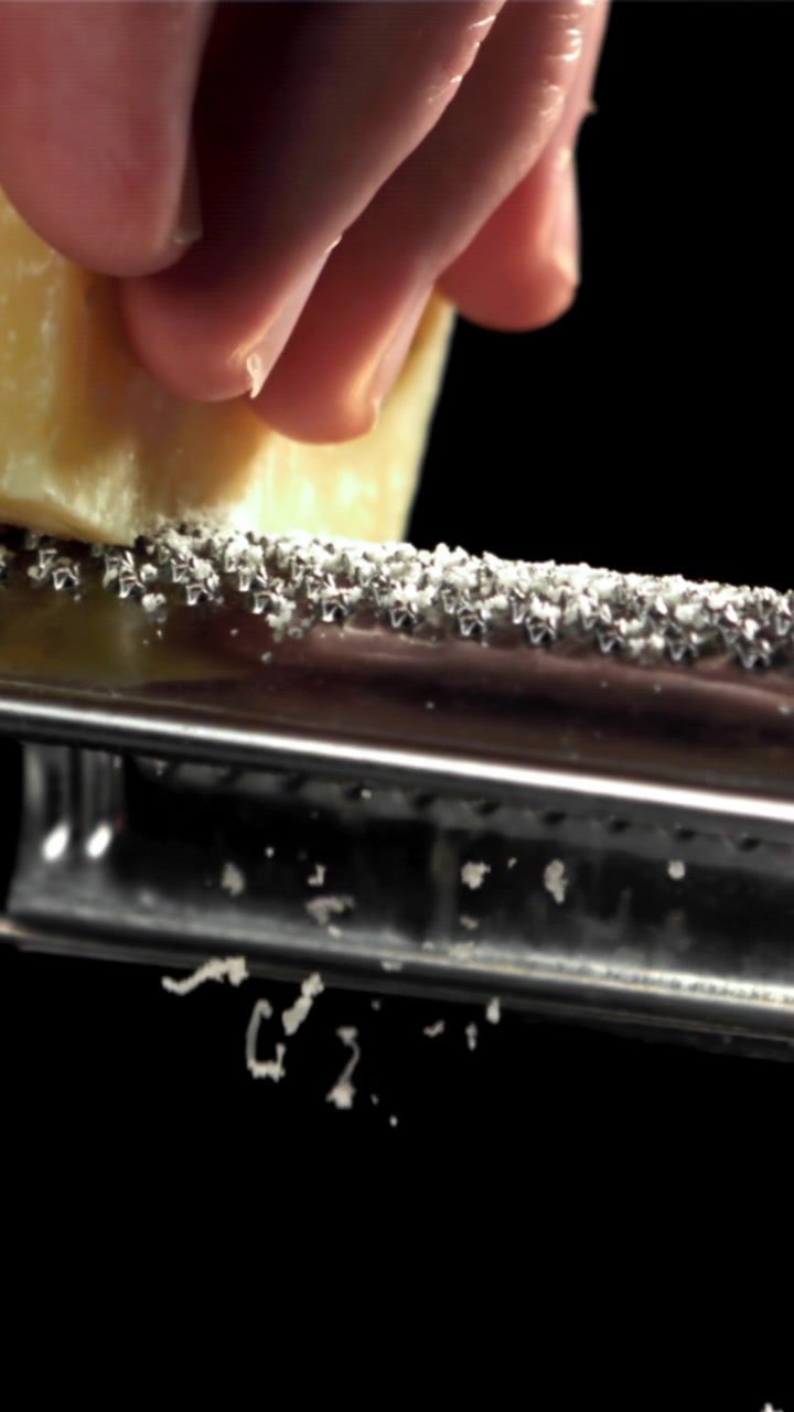 Primo piano di una mano che grattugia Parmigiano Reggiano al rallentatore