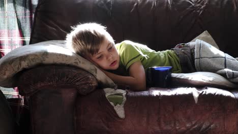 young boy lying resting on torn damaged comfortable sofa couch relaxing furniture