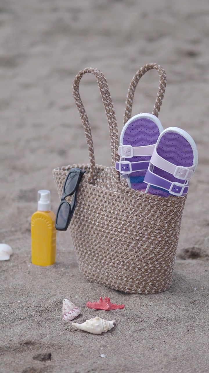 Beach Bag with Sandals and Sunscreen on Sandy Shore