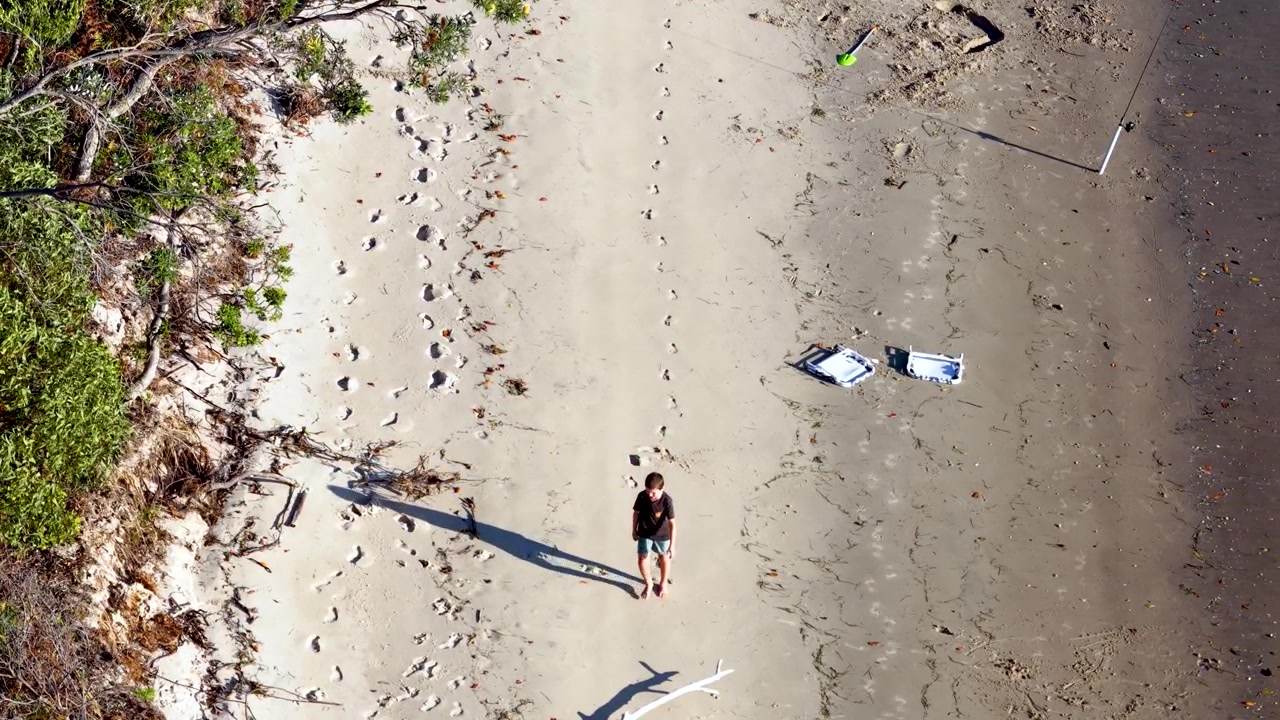 Ripresa aerea con drone di un ragazzo che cammina lungo una costa sabbiosa a South Stradbroke, Australia
