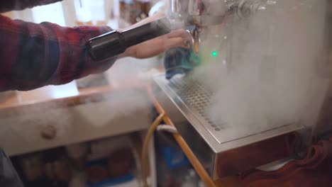 barista cleans steam wand of coffee machine with cloth and steam