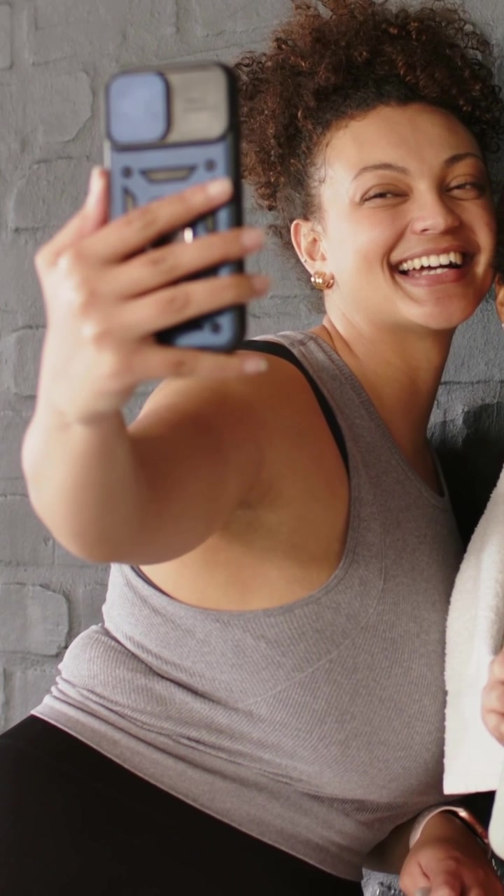 Video verticale: Chi si fa un selfie si appoggia e angola il braccio, inquadrando un selfie in palestra con custodia blu, asciugamano e bottiglia.